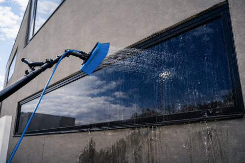 Cleaning a large window with a water fed pole, blue brush and blue hose