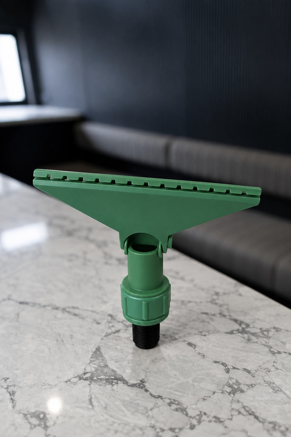 Green Fixi clamp for a water fed pole with its jaws closed on a marble benchtop